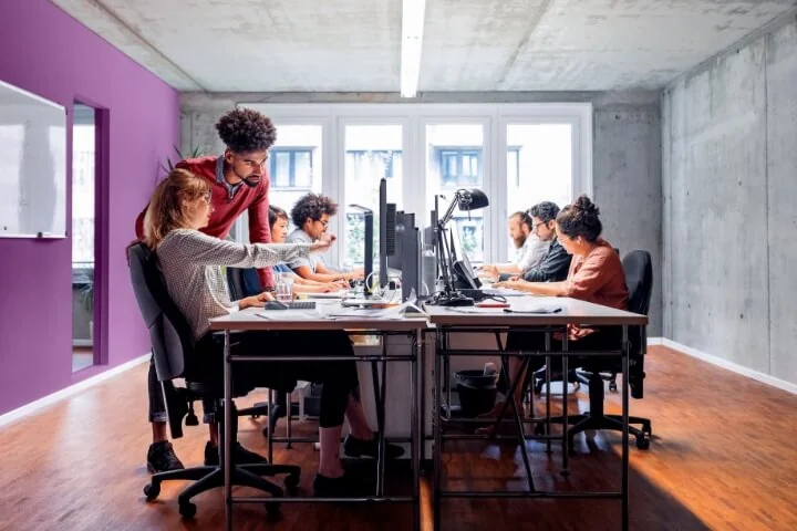Equipo de trabajo en una oficina abierta, frente a PCs y monitores